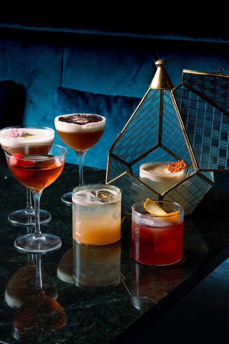 Array of cocktails on a marbled table and blue sofa background at Queen’s Tandoor Indian Restaurant Bali